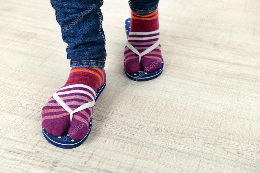 Female feet in socks with pink flip-flops, on floor background