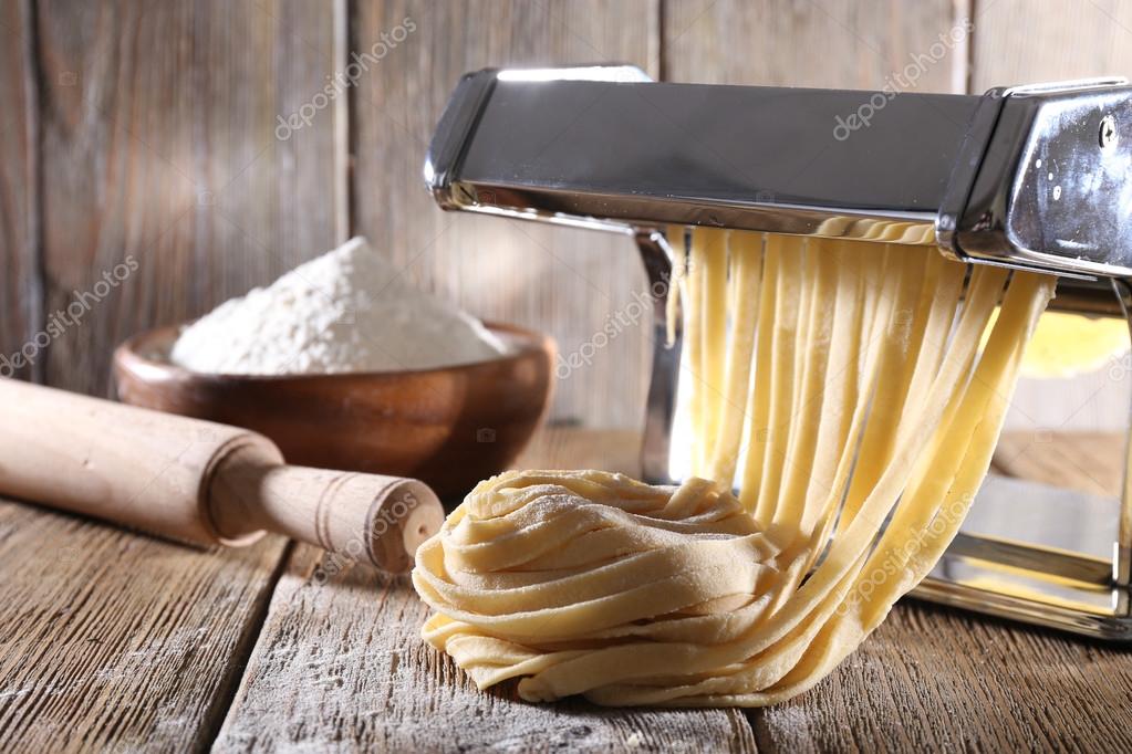 Fare tagliatelle con macchina per pasta su sfondo di legno Foto Stock