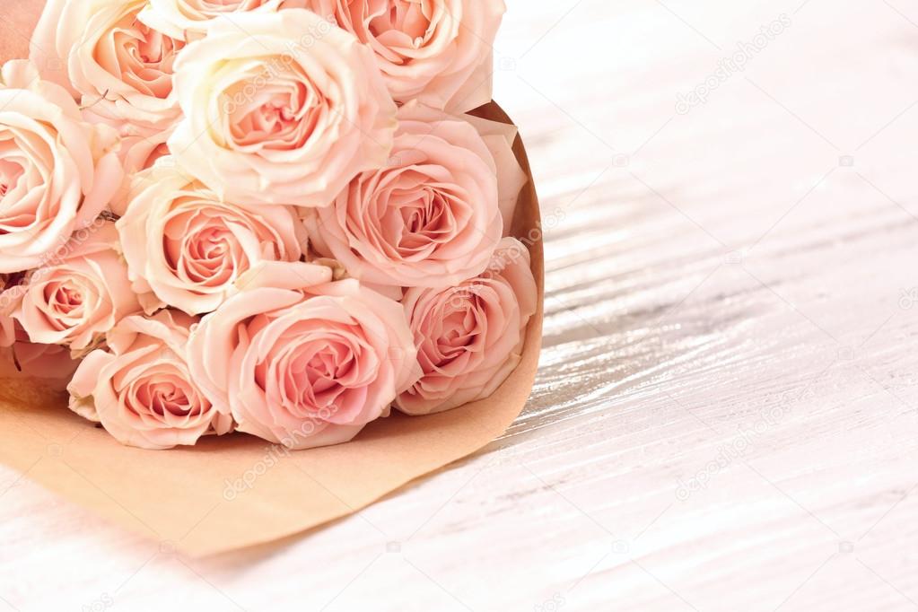 Bouquet of fresh roses wrapped in paper on wooden background