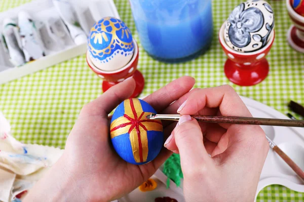 Молодая женщина рисует пасхальные яйца на столе вблизи — стоковое фото