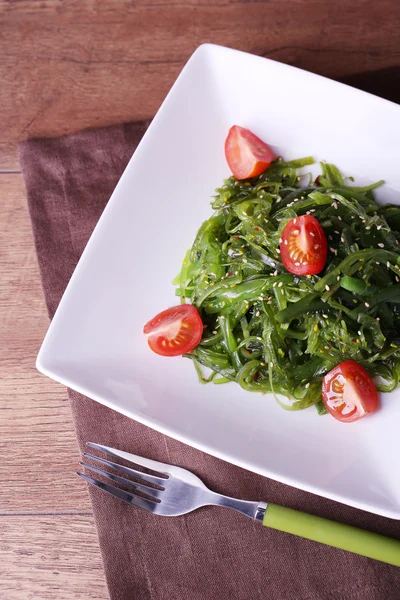 Algensalat mit Kirschtomatenscheiben im Teller auf Serviette und Holztischhintergrund — Stockfoto