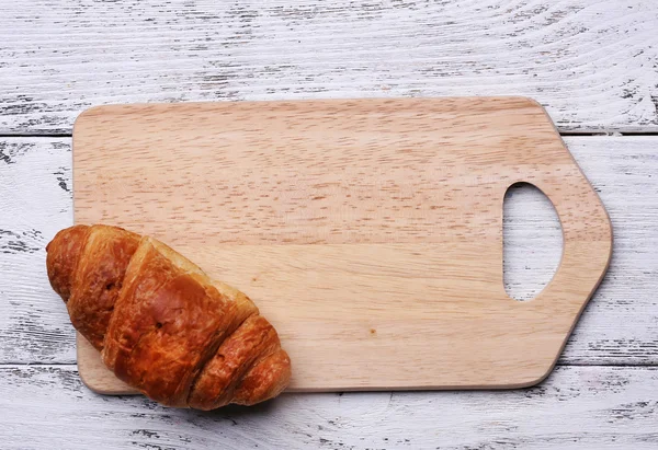 Cutting board with croissant on color wooden planks background — Stock Photo, Image