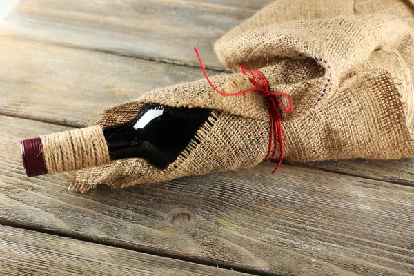 Bouteille de vin rouge enveloppée dans un tissu de toile de jute sur des planches en bois — Photo