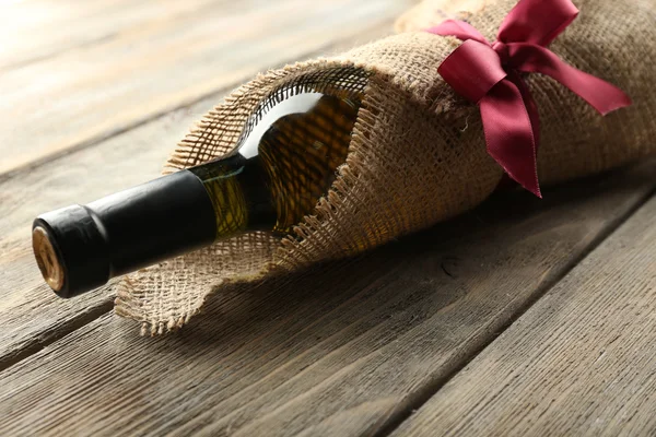 Botella de vino envuelta en tela de arpillera sobre tablones de madera fondo — Foto de Stock