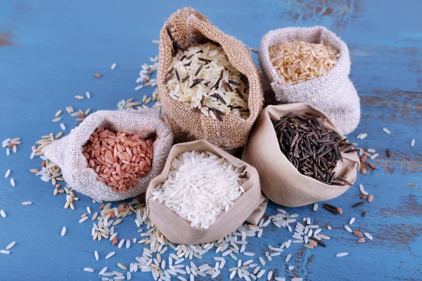 Diferentes tipos de arroz em sacos no fundo de madeira — Fotografia de Stock