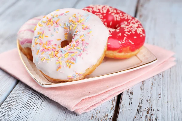 Deliciosas rosquillas con hielo en la placa sobre fondo de madera —  Fotos de Stock