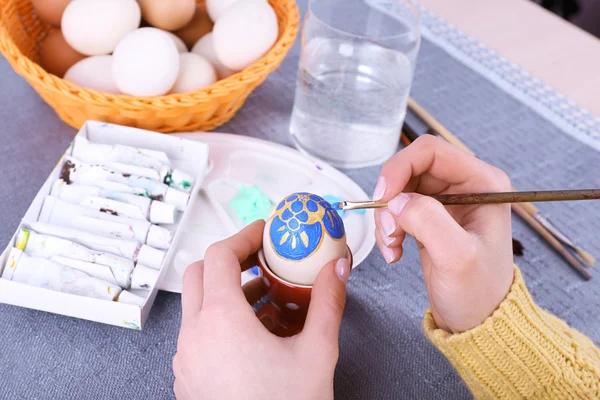 Painting Easter eggs by female hands on colorful tablecloth background — Stock Photo, Image