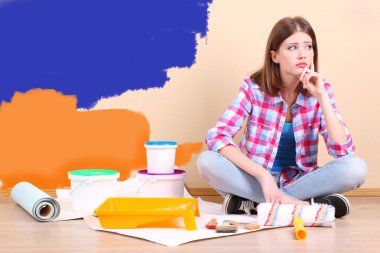 Güzel kız boyama duvar için ekipman ile katta oturan