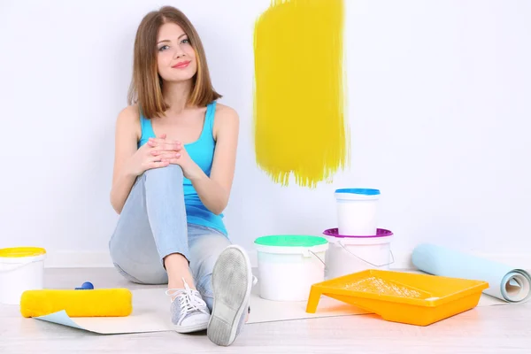 Красивая девушка сидит на полу с оборудованием для покраски стены — стоковое фото