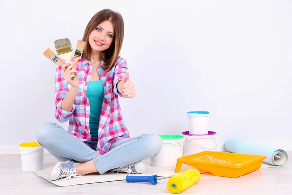 Beautiful girl sitting on floor with equipment for painting wall — Stock Photo, Image