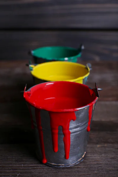 Metal buckets with colorful paint on wooden background — Stock Photo, Image