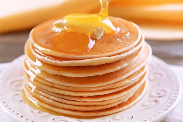 Deliciosos panqueques con miel en el plato en primer plano de la mesa — Foto de Stock