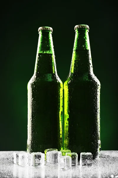 Garrafas de vidro de cerveja com cubos de gelo em fundo verde escuro — Fotografia de Stock