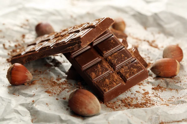 Pieces of chocolate with cocoa on parchment, closeup — Stock Photo, Image