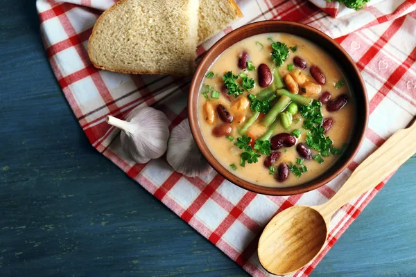 Zuppa di fagioli in ciotola con pane fresco tagliato a fette su tovagliolo, su sfondo tavolo di legno — Foto Stock