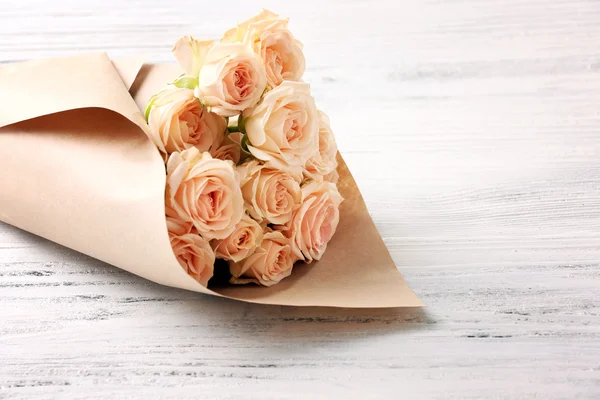Bukett färska rosor inslagna i papper på trä bakgrund — Stockfoto