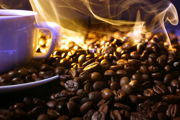 Pilha de grãos de café e xícara de café quente em feixe no fundo escuro — Fotografia de Stock