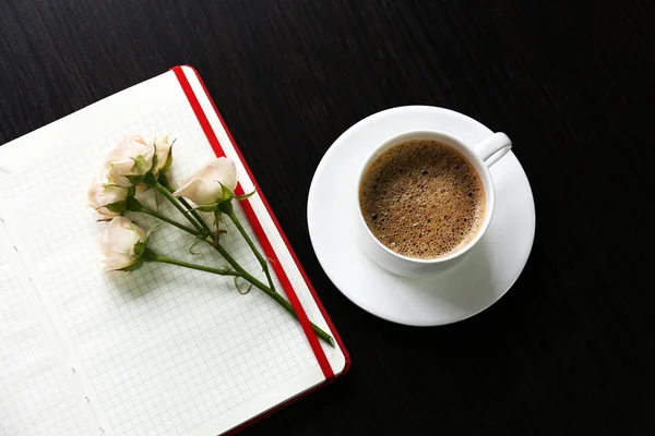 Kopp kaffe med anteckningsboken och färska blommor på träbord bakgrund — Stockfoto