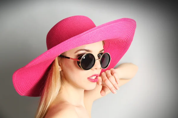 Pembe şapka ile güneş gözlüğü gri arka plan üzerinde etkileyici genç modeli — Stok fotoğraf