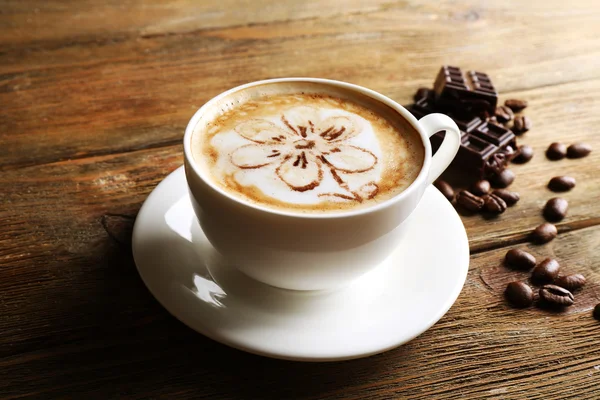 Cup of coffee latte art with grains and chocolate on wooden background — Stock Photo, Image