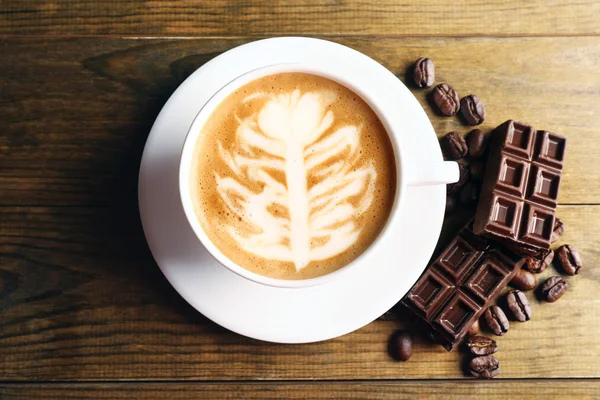 Cup of coffee latte art with grains and chocolate on wooden background — Stock Photo, Image