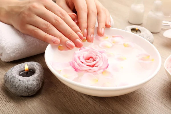 Vrouwelijke handen en kom met spa water met bloemen, close-up — Stockfoto