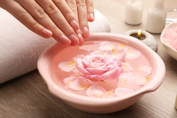 Mãos femininas e tigela de água termal com flores, close-up — Fotografia de Stock