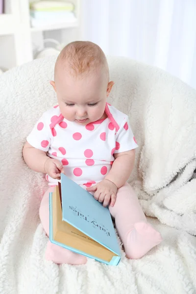 Menina bonito sentado em cadeira de braço com livro, em casa fundo interior — Fotografia de Stock