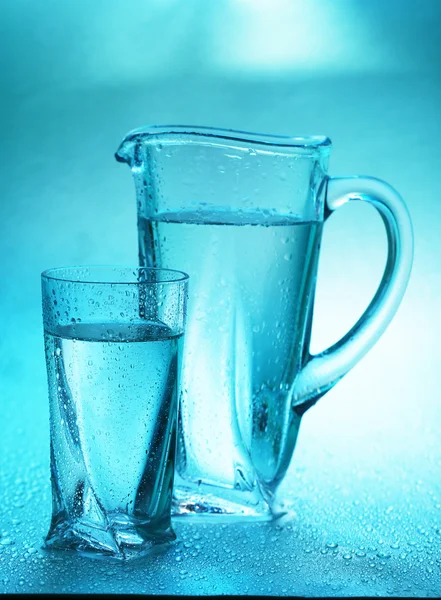 Jarra de vidrio y vaso de agua sobre fondo azul —  Fotos de Stock