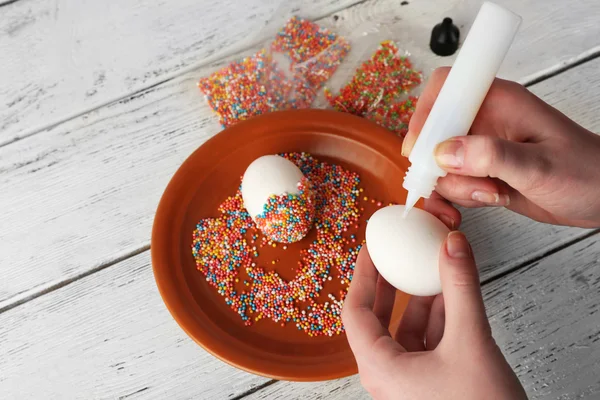 Woman decorating Easter eggs on wooden table, closeup — Stock Photo, Image