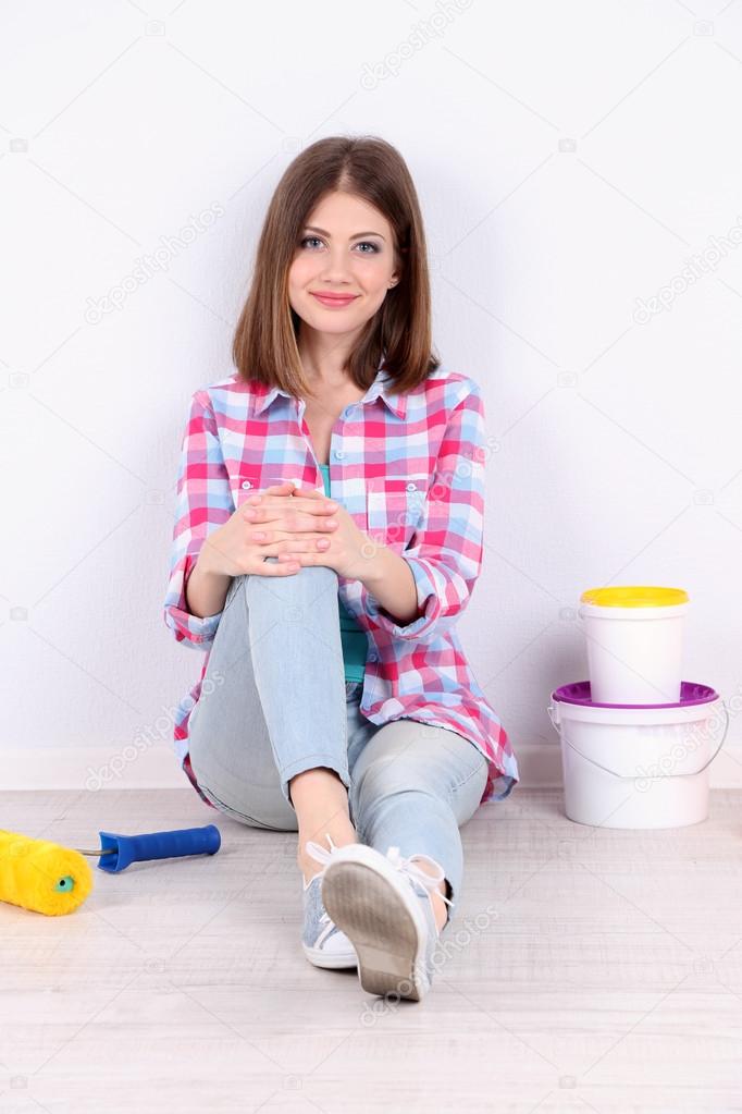Beautiful girl sitting on floor with equipment for painting wall