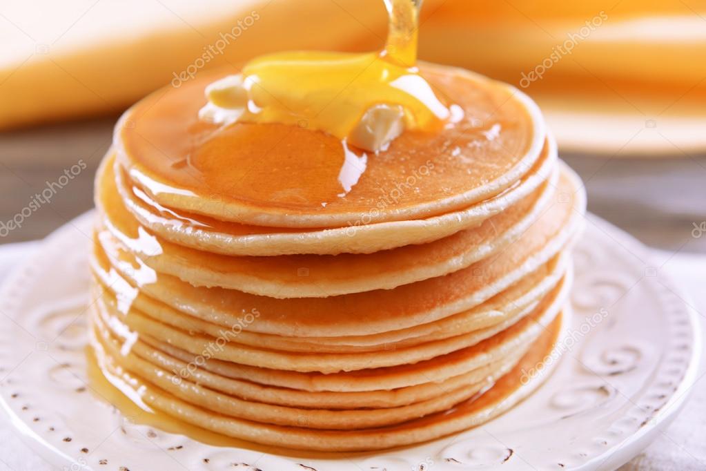 Delicious pancakes with honey on plate on table close-up