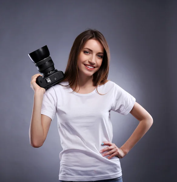 Young female photographer taking photos on grey background — Stock Photo, Image