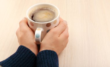 Kadın elleri bir fincan kahve tutuyor.