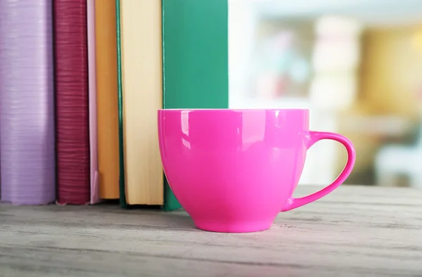 Renkli bardak içki kitapları ahşap yüzey ve ışık arka plan ile — Stok fotoğraf