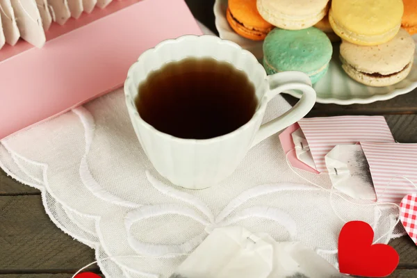 Herzförmige Teebeutelanhänger, Makronen und Tasse Tee auf Holzgrund — Stockfoto