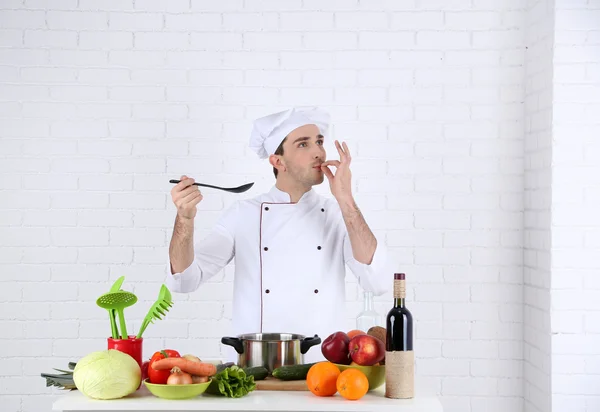 Chef en la mesa con diferentes productos y utensilios en la cocina sobre fondo blanco de la pared — Foto de Stock