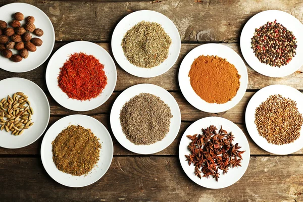 Different spices on plates, on old wooden table — Stock Photo, Image