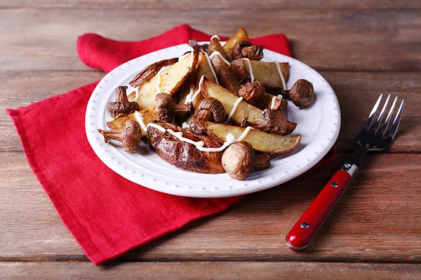 Baked potatoes with mushrooms and sauce on plate on wooden table — Stock Photo, Image