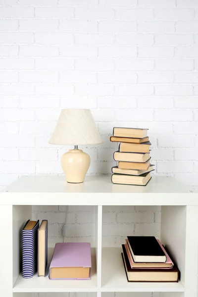 Prateleira de madeira com livros e lâmpada no fundo da parede de tijolo — Fotografia de Stock