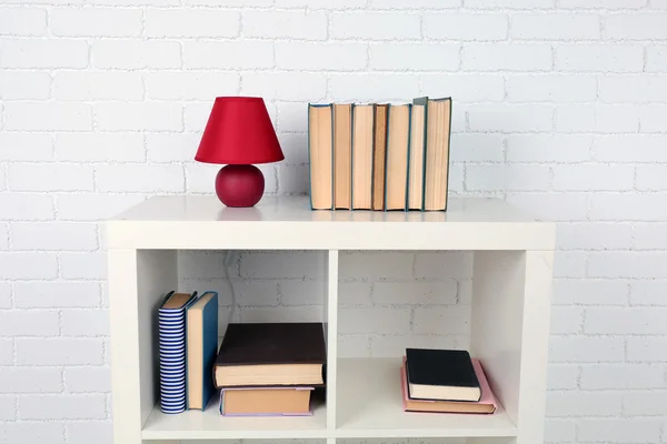 Estante de madera con libros y lámpara sobre fondo de pared de ladrillo —  Fotos de Stock