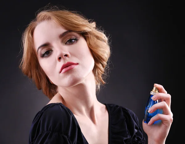 Piękna młoda kobieta z butelki perfum na czarnym tle — Zdjęcie stockowe
