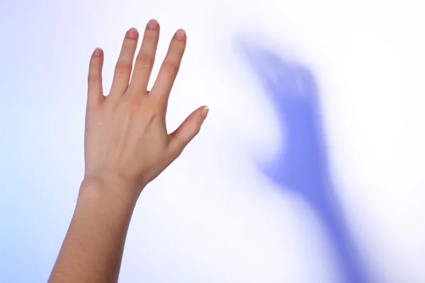 Mano femminile e ombra blu su sfondo colorato luce — Foto Stock