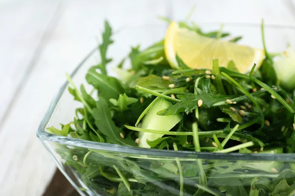 Glass bowl of green salad on wooden table, closeup — Stock Photo, Image