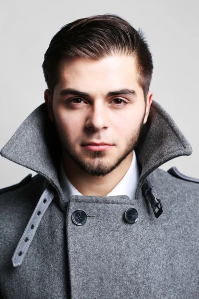 Young man in coat on gray background — Stock Photo, Image