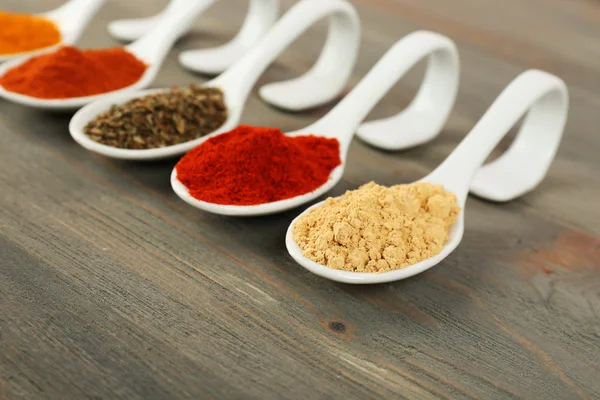 Different kinds of spices in spoons on wooden background — Stock Photo, Image