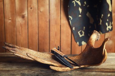 Moose antler with hunting knives on wooden background clipart