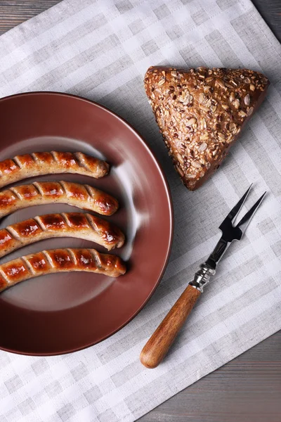 Grilled sausages on plate with bread on table close up — Stock Photo, Image