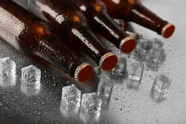 Bottiglie di vetro di birra con cubetti di ghiaccio su sfondo tavolo bagnato — Foto Stock