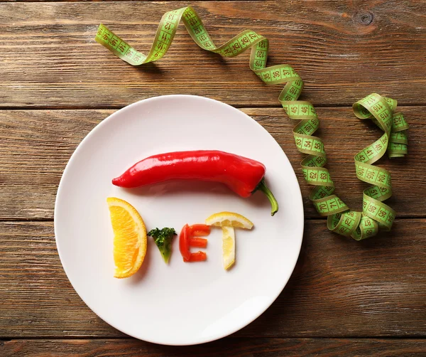 Słowo dieta wykonane w plasterkach warzywa w białe płytki z Miara zwijana na drewnianym stole, widok z góry — Zdjęcie stockowe